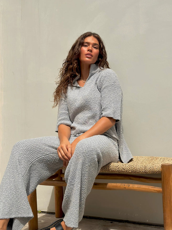 Woman seated on bench in gray knit lounge set.