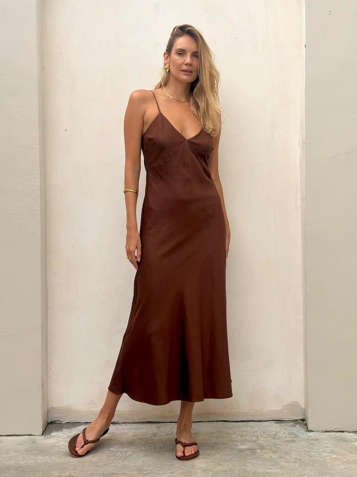 Woman in brown satin slip midi dress with thin straps.