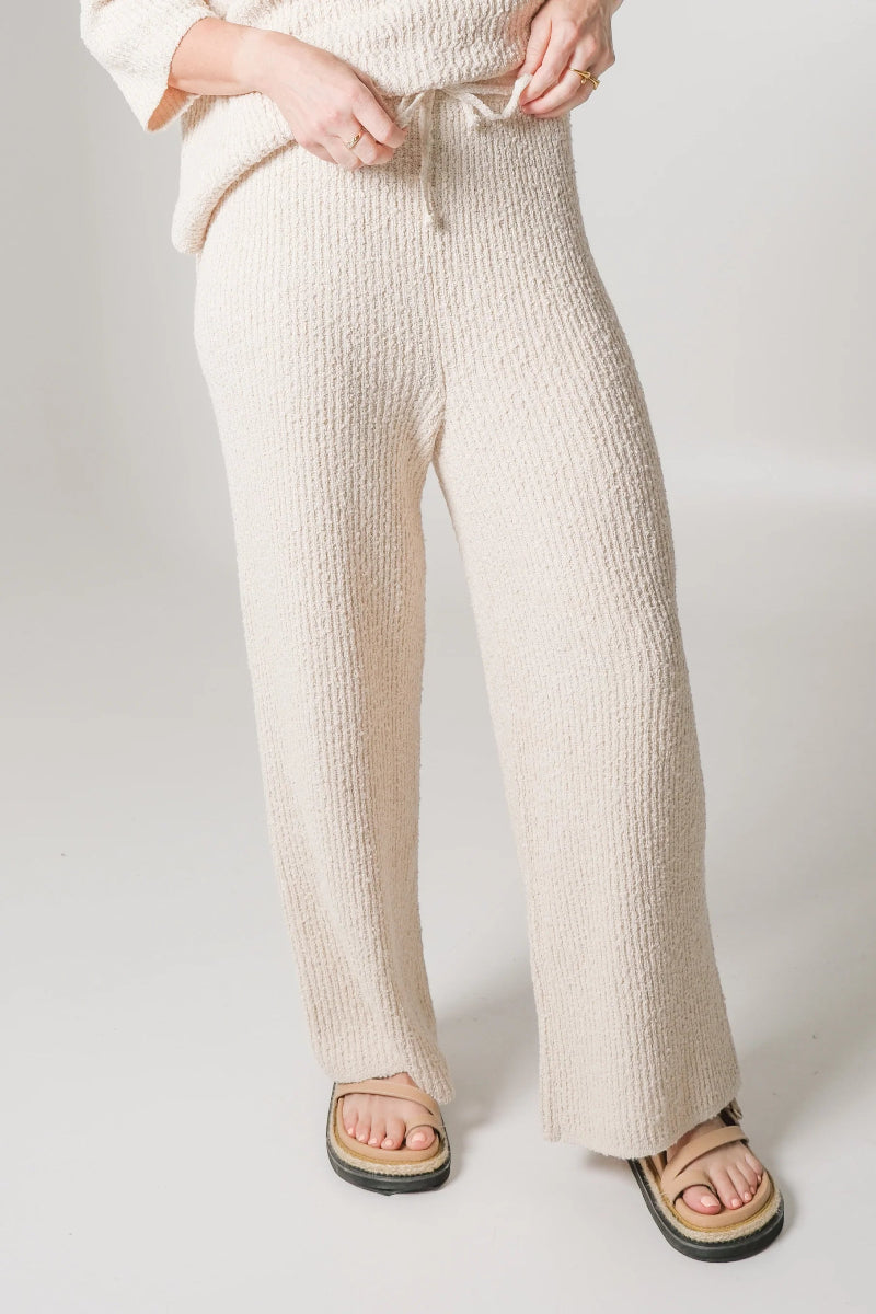 Close-up of cream knit pants with drawstring and sandals.