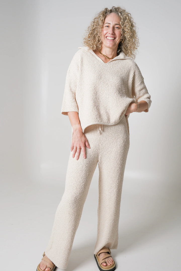 Smiling woman in cream knit lounge set on white background.