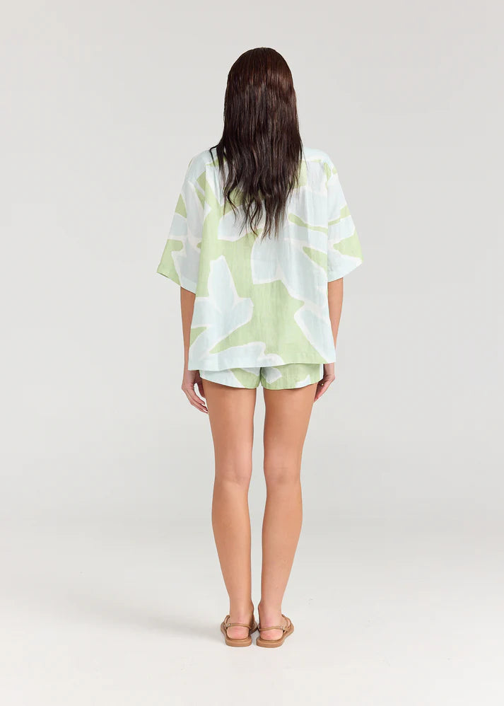 Person wearing a light green and white patterned shirt and shorts on a plain background