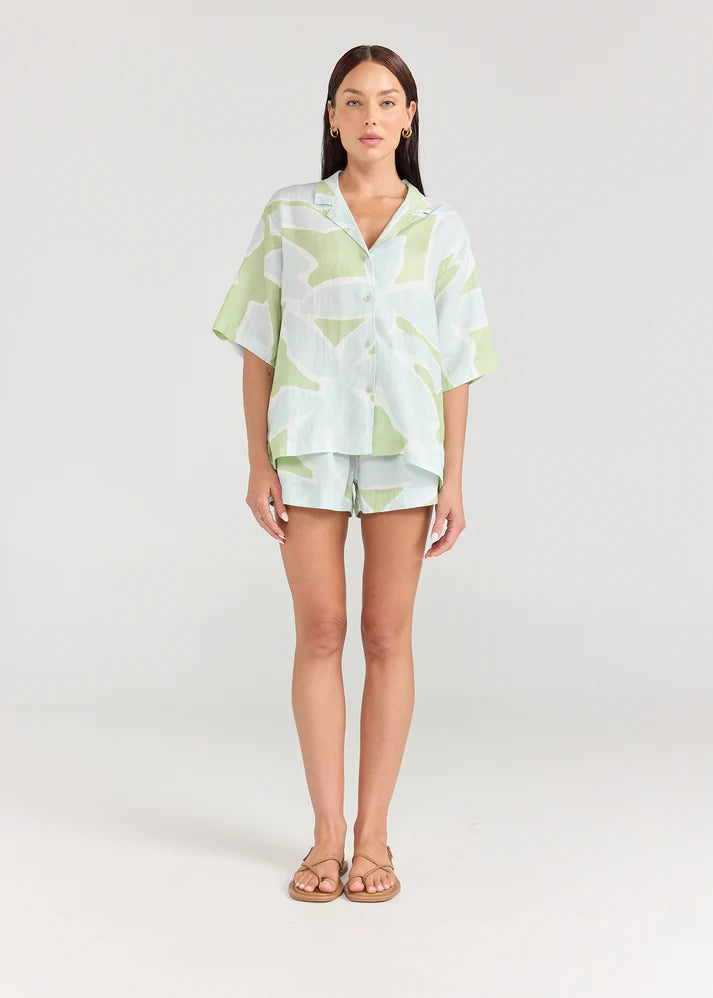 Woman wearing a light green and white patterned outfit on a plain background