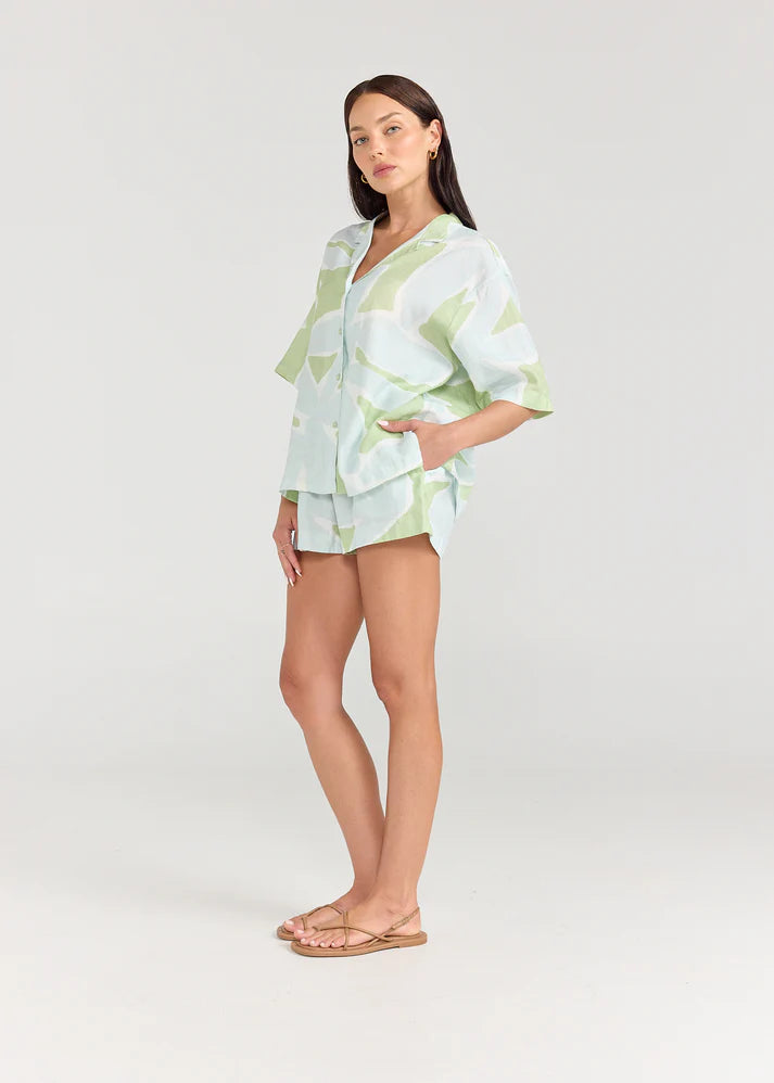 Woman wearing a light green and white patterned outfit on a plain background