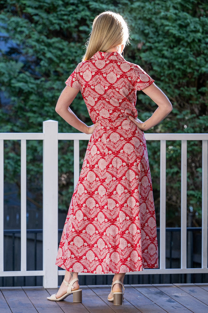 Woman wearing a red, floral patterned maxi dress standing on a wooden deck with greenery in the background