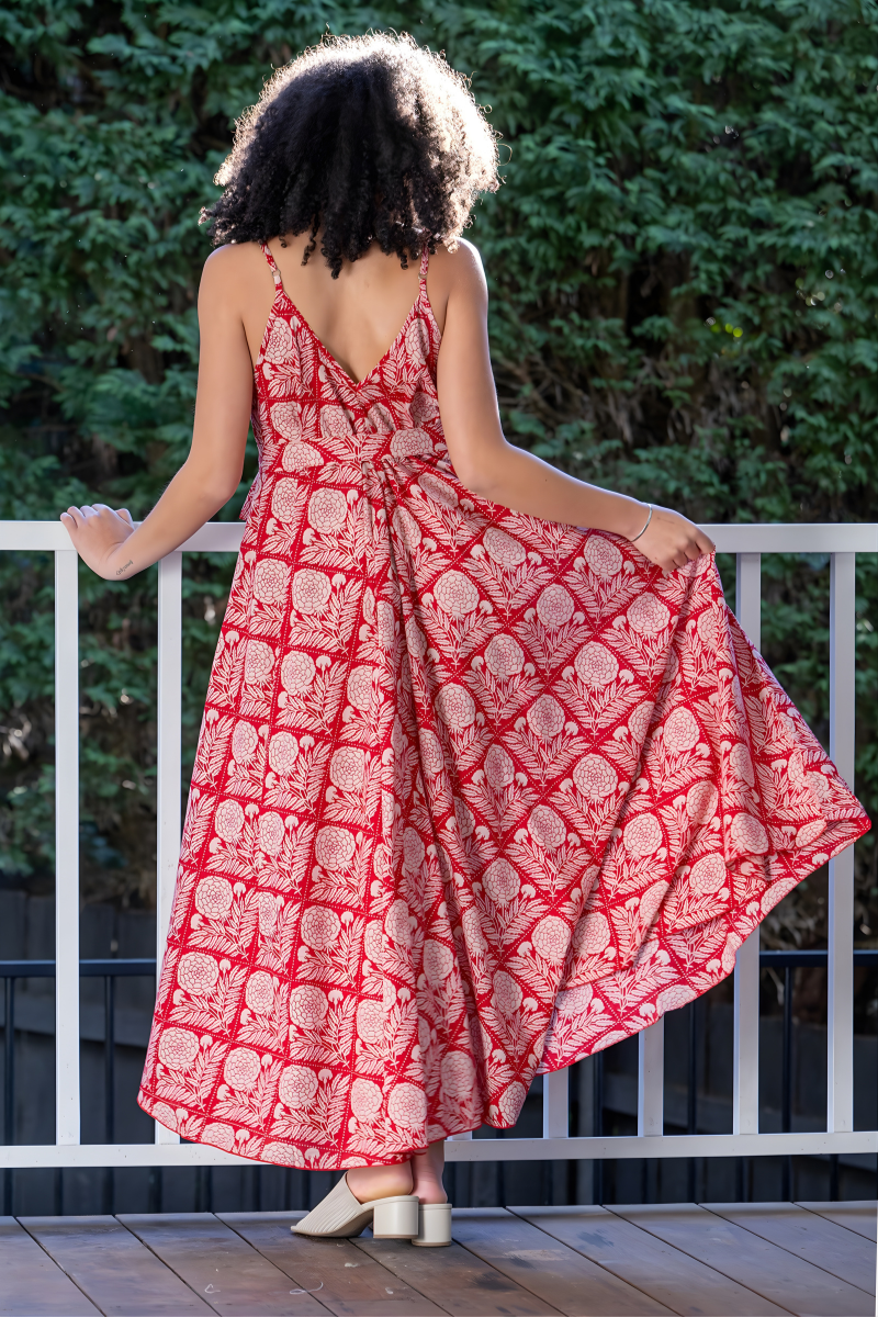 Woman wearing a red and white, floral patterned maxi dress standing on a wooden deck with greenery in the background.