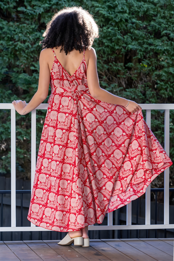 Woman wearing a red and white, floral patterned maxi dress standing on a wooden deck with greenery in the background.