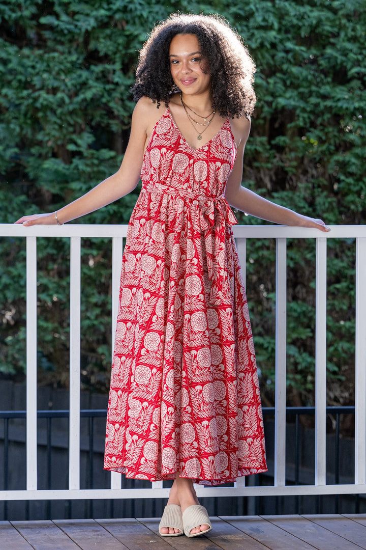 Woman wearing a red and white, floral patterned maxi dress standing on a deck with greenery in the background
