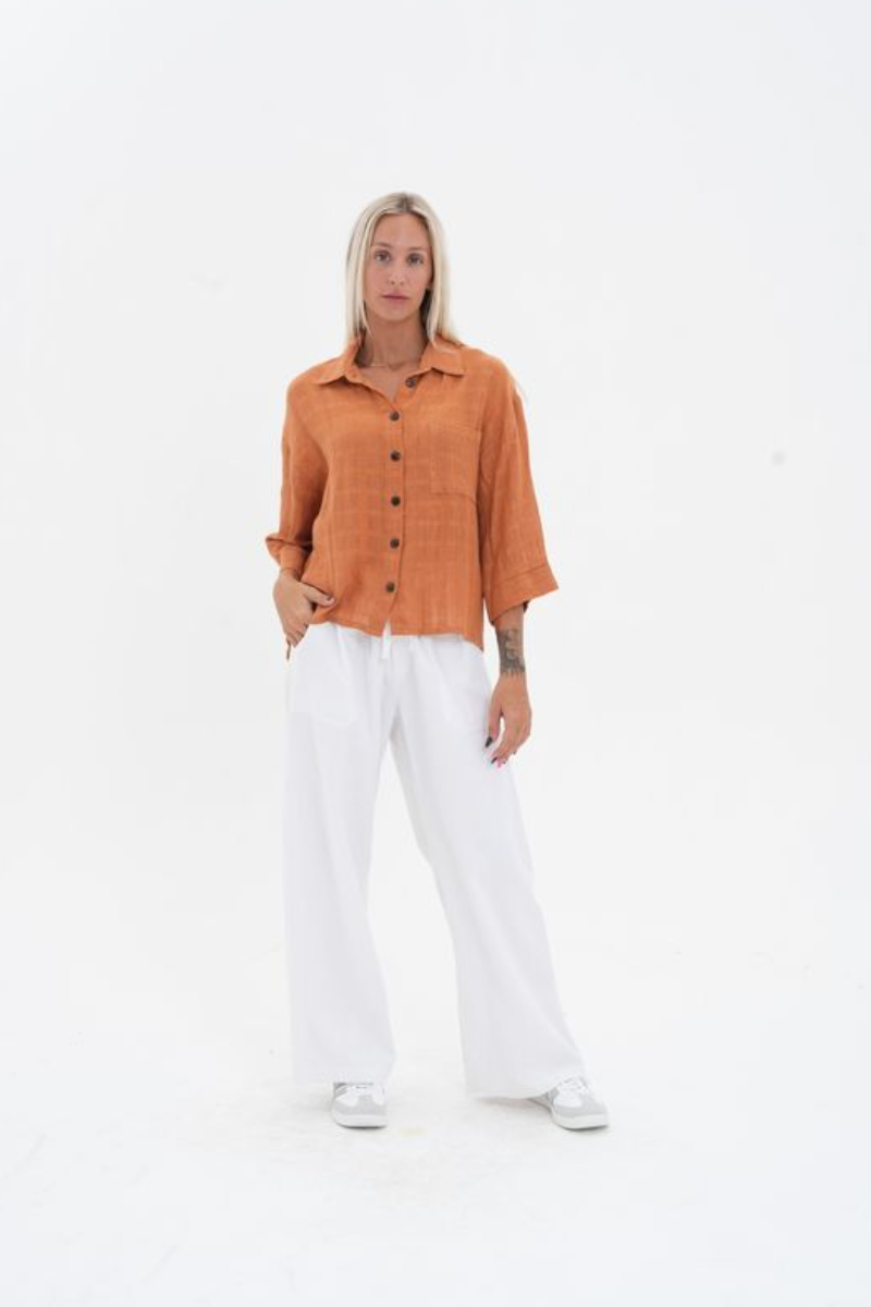 Woman wearing an orange button-up shirt and white pants on a white background