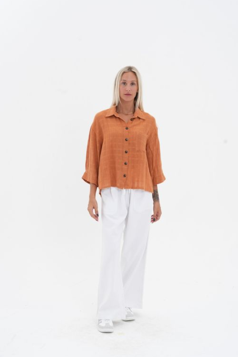 Person wearing an orange button-up shirt and white pants on a white background