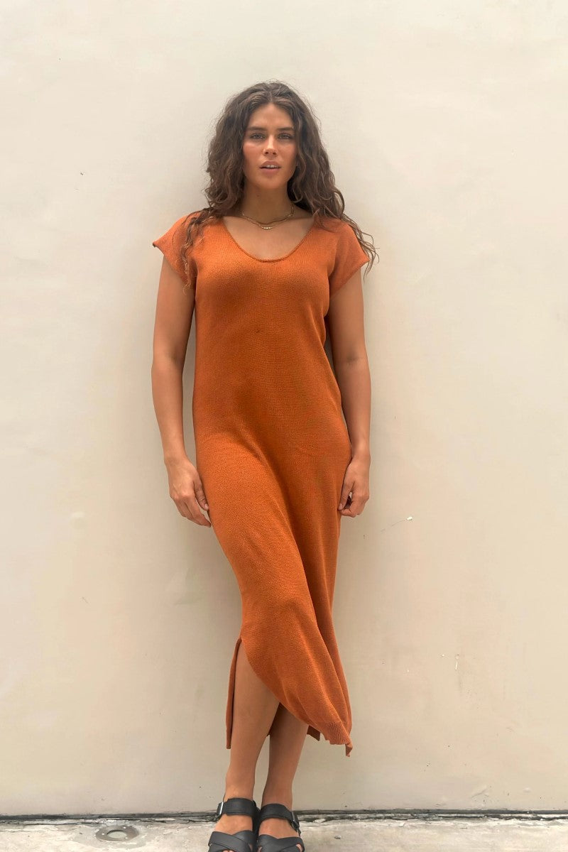 Woman wearing an orange dress against a plain wall