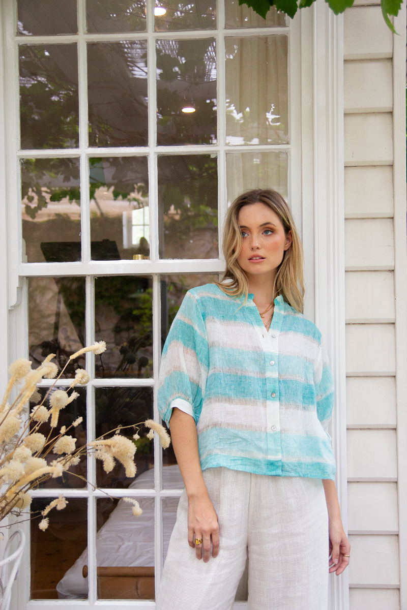 Woman wearing a light blue and white striped shirt standing in front of a window.