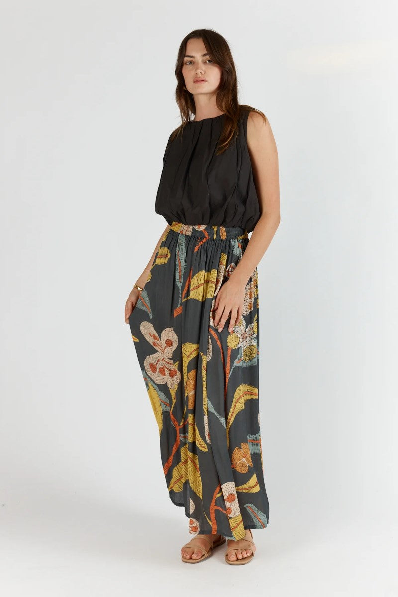 Woman wearing a black sleeveless top and floral-patterned pants on a white background