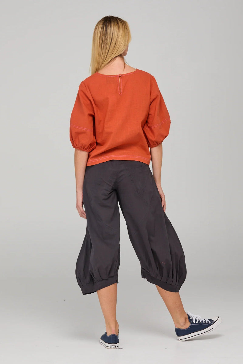 Person wearing an orange top and black pants on a gray background