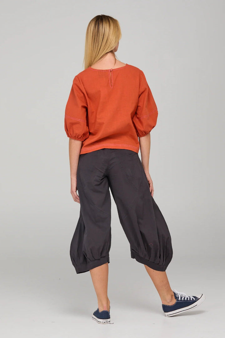 Person wearing an orange top and black pants on a gray background