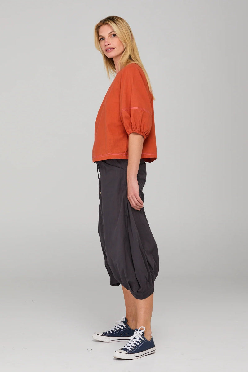 Woman wearing an orange top and black pants on a plain background