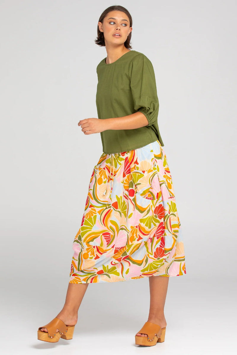 Woman wearing a green top and colorful floral skirt on a white background