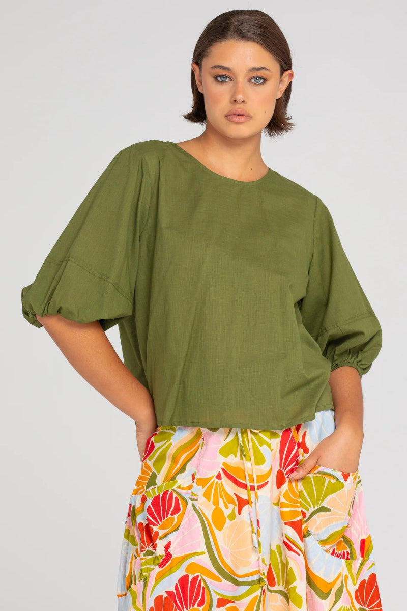 Woman wearing a green top and colorful floral pants on a plain background