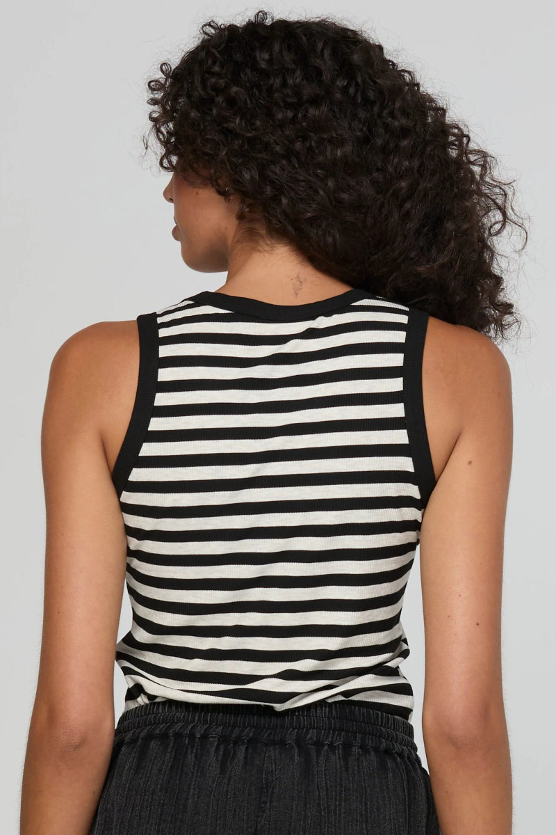 A woman shown from the back wearing a black and white horizontally striped sleeveless tank top and dark gray textured pants, set against a solid light gray studio background.
