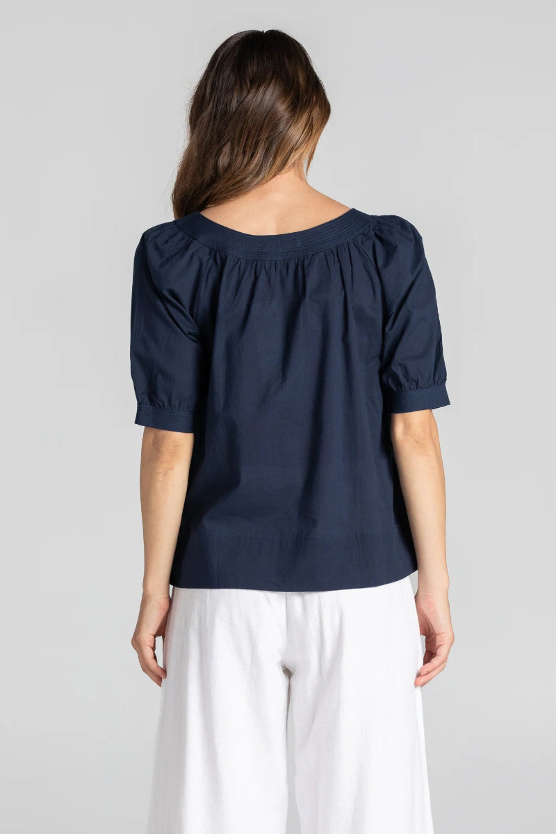 Person wearing a navy blue blouse with white pants on a gray background