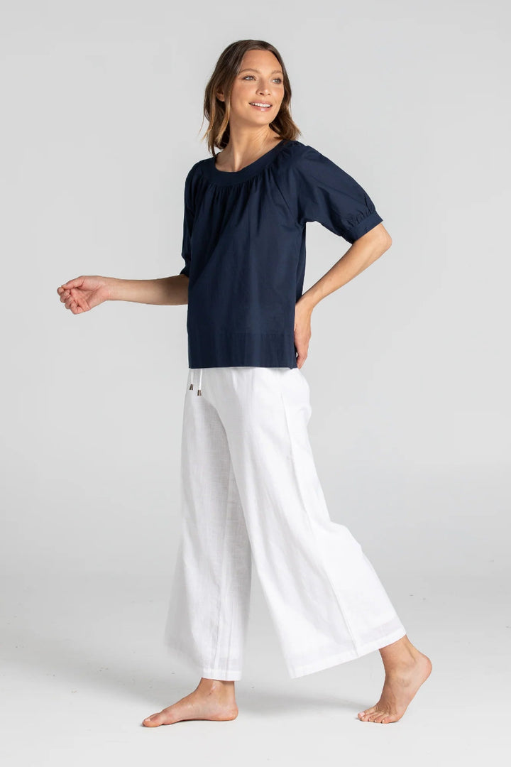 Woman wearing a navy top and white pants on a light gray background