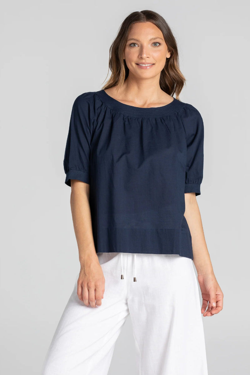 Woman wearing a navy blue blouse and white pants on a gray background