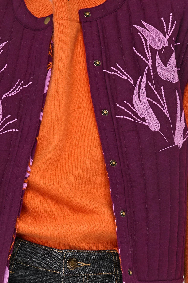 Close-up of a purple cardigan with floral patterns over an orange shirt.