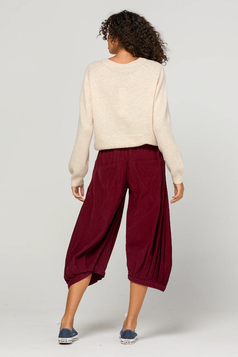 Person wearing a cream sweater and burgundy pants on a plain background