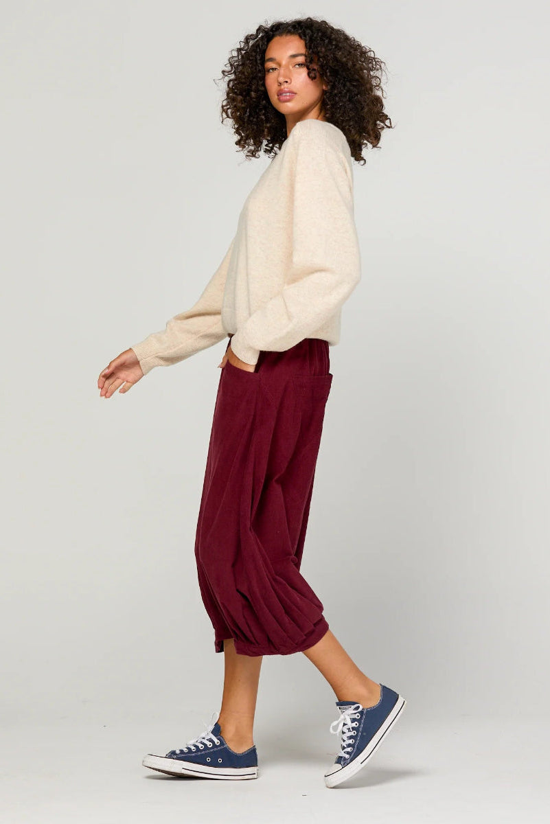 Woman wearing a cream sweater and burgundy pants with navy sneakers on a light gray background