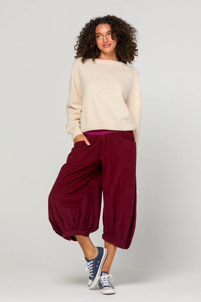 Woman wearing a cream sweater and burgundy pants on a plain background