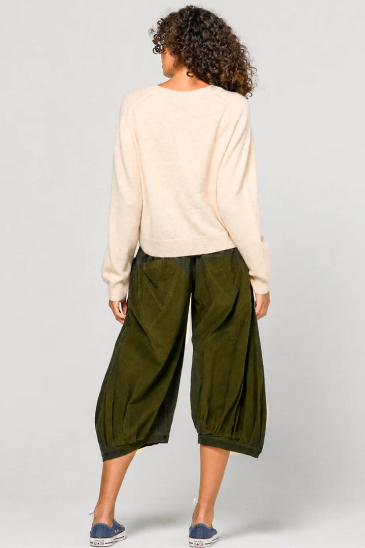 Person wearing a beige sweater and green wide-leg pants on a plain background
