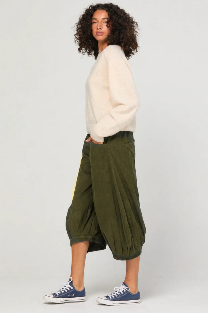 Woman wearing a white sweater and green pants on a plain background