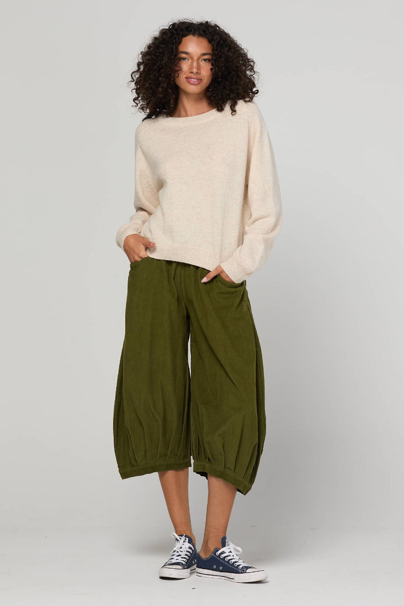 Woman wearing a beige sweater and green pants on a white background