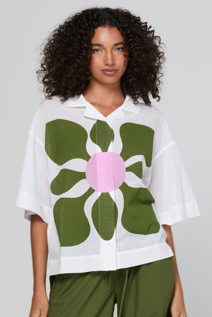 Woman wearing a white shirt with a large green flower design on a plain background