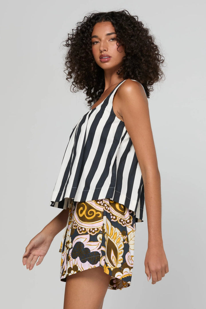A woman modeling a sleeveless top and shorts set against a plain light gray studio background. The top has vertical black and white stripes, while the shorts feature a multicolor paisley and floral pattern in yellow, brown, black, and white.