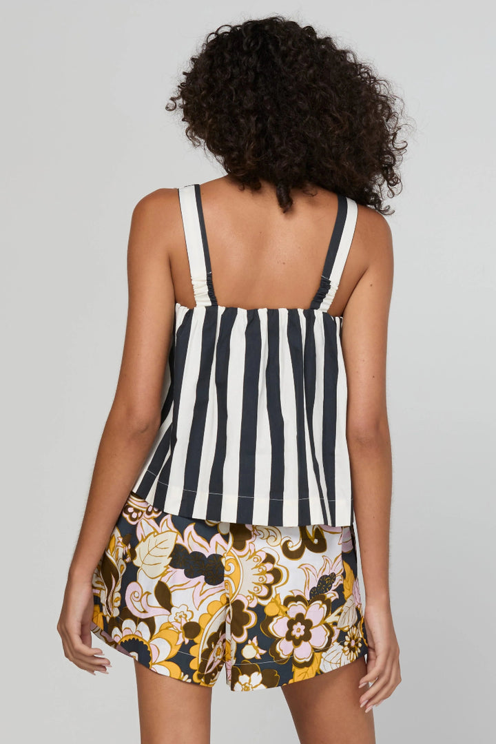 A woman shown from the back wearing a sleeveless striped top with black and white vertical stripes and floral print shorts with yellow, black, and white patterns, set against a plain light gray studio background.