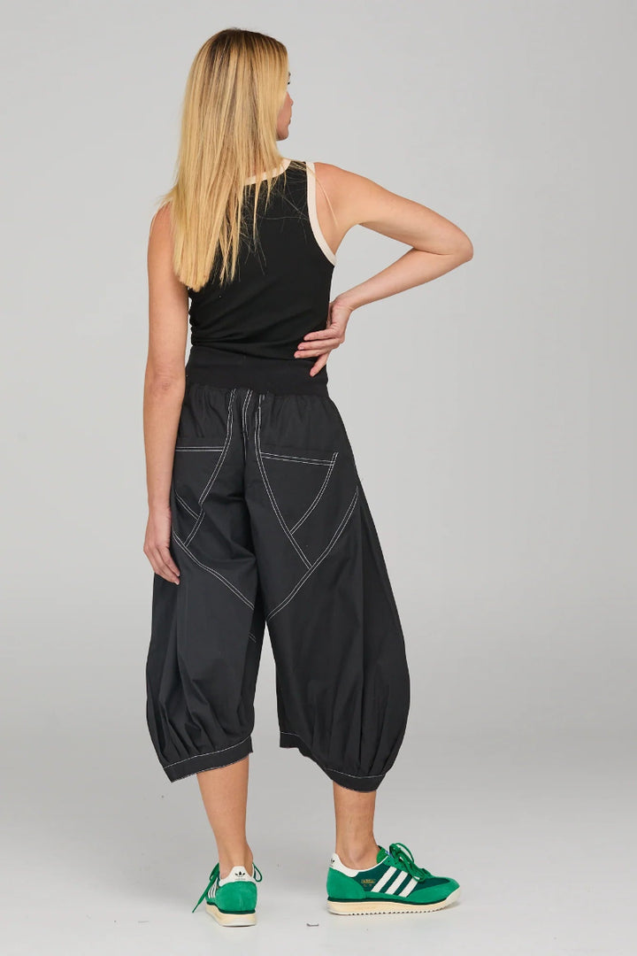 Woman wearing black capri pants with white stitching on a gray background