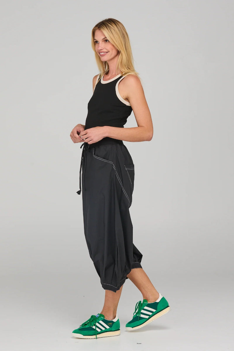 Woman wearing a black sleeveless top and gray capri pants with green Adidas sneakers on a light gray background