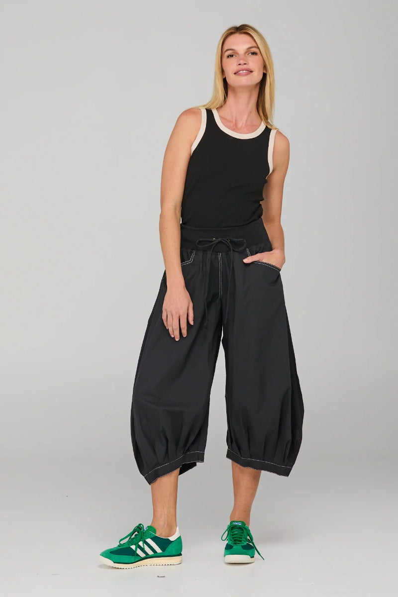 Woman wearing a black sleeveless top and wide-leg pants with green sneakers on a gray background