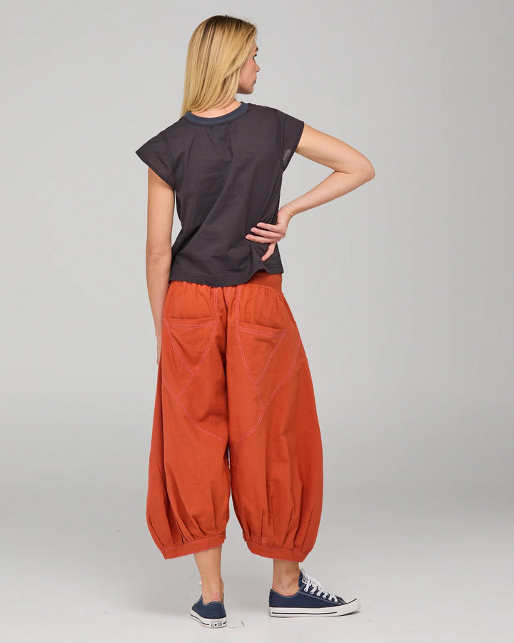 Woman wearing a dark gray top and orange pants on a plain background