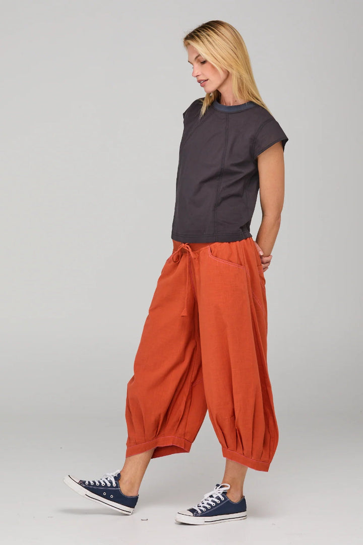 Woman wearing a dark gray t-shirt and orange harem pants on a plain background