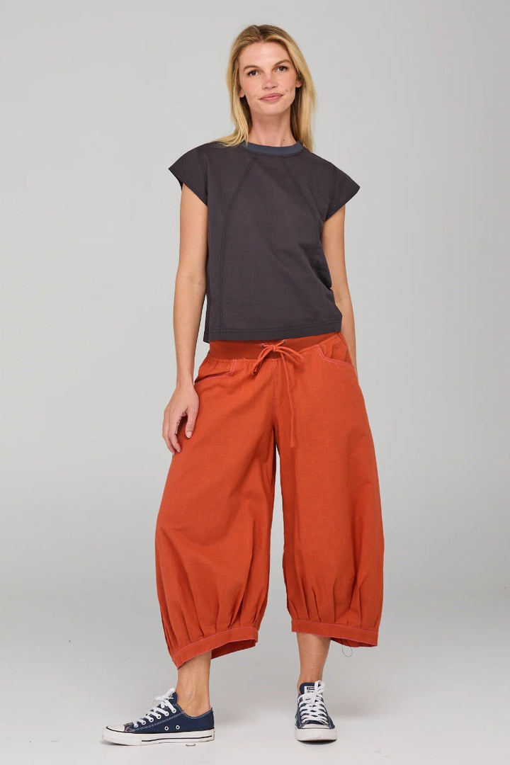 Woman wearing a dark top and orange pants on a gray background
