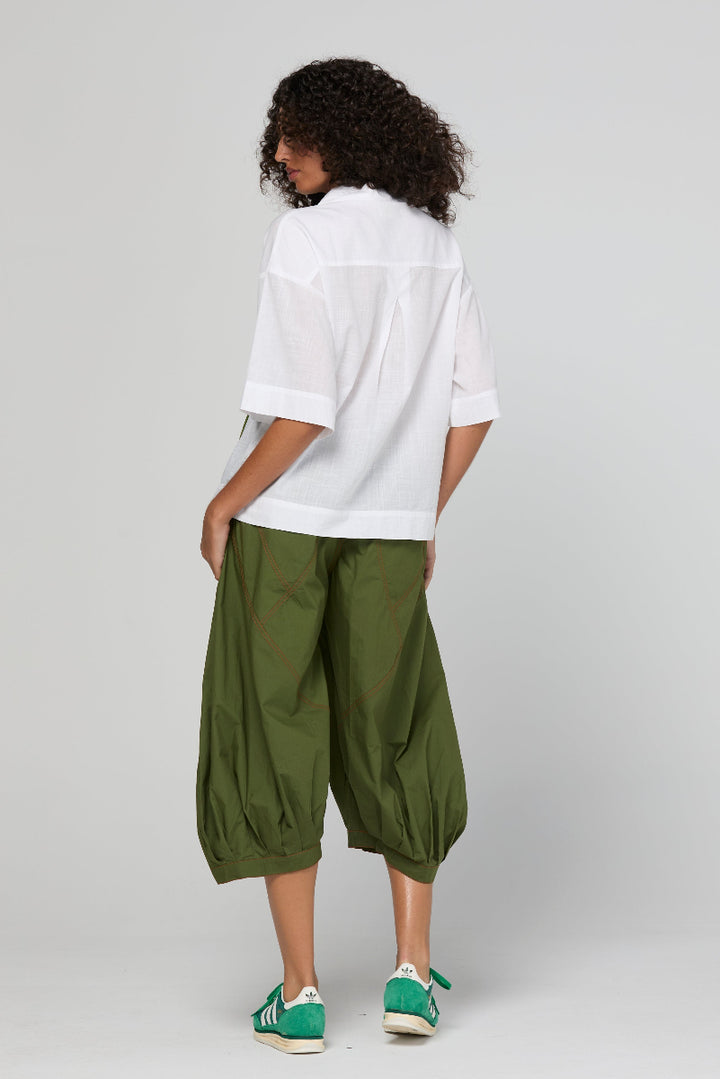 Person wearing a white shirt and green pants on a plain background