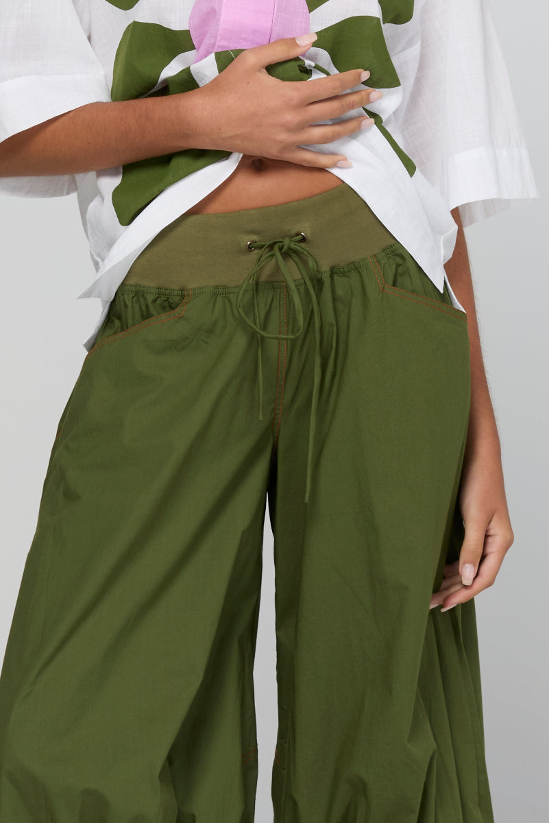 Person wearing green wide-leg pants and a white top with a floral pattern on a light gray background