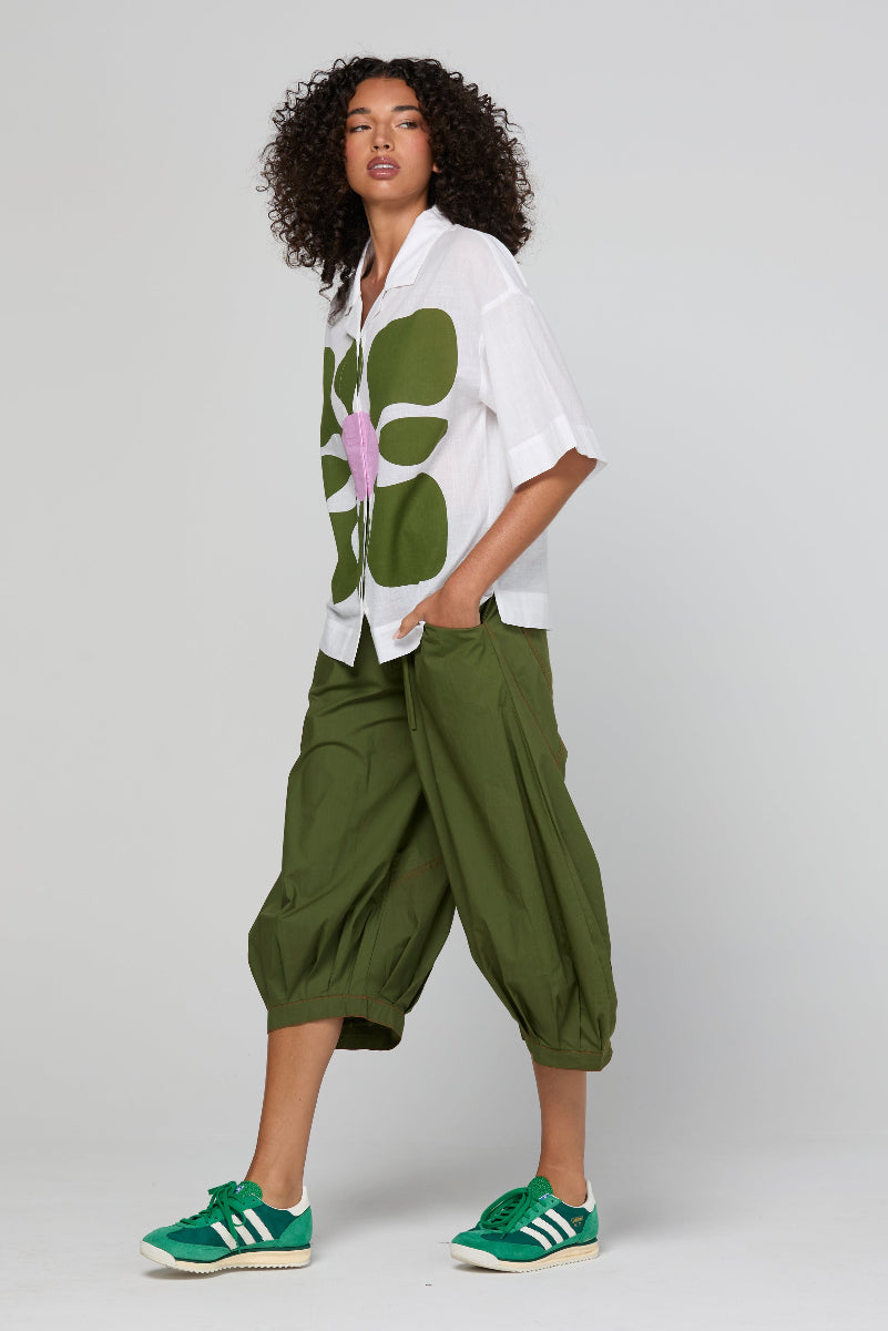 Woman wearing a white shirt with a green floral pattern and green pants on a plain background