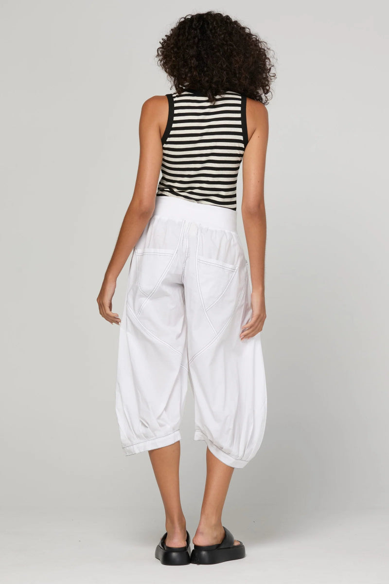 A model viewed from the back wearing a black and white striped sleeveless top and white baggy cropped pants, paired with black flat shoes, against a light gray studio background.