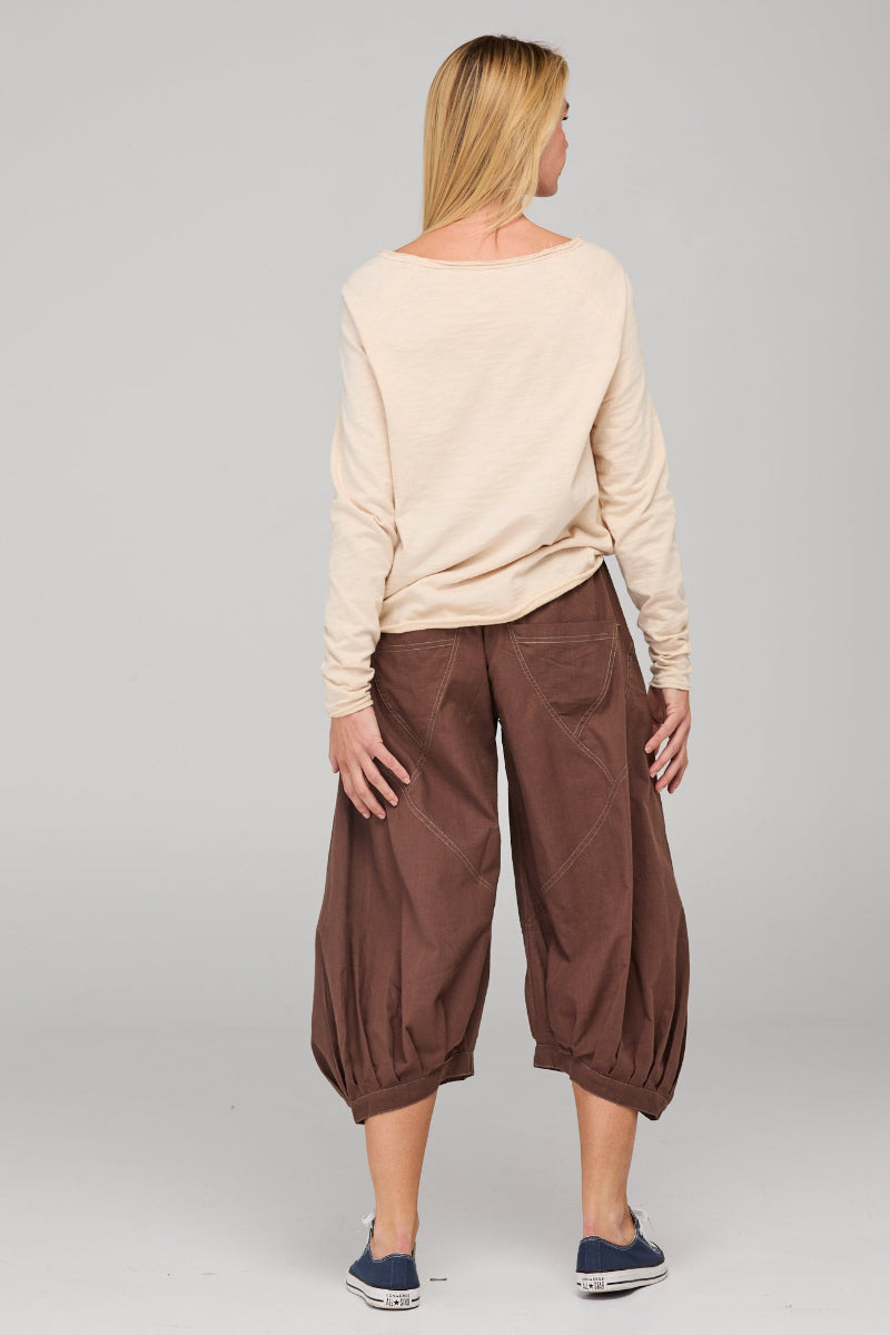 Woman wearing a beige sweater and brown pants on a plain background