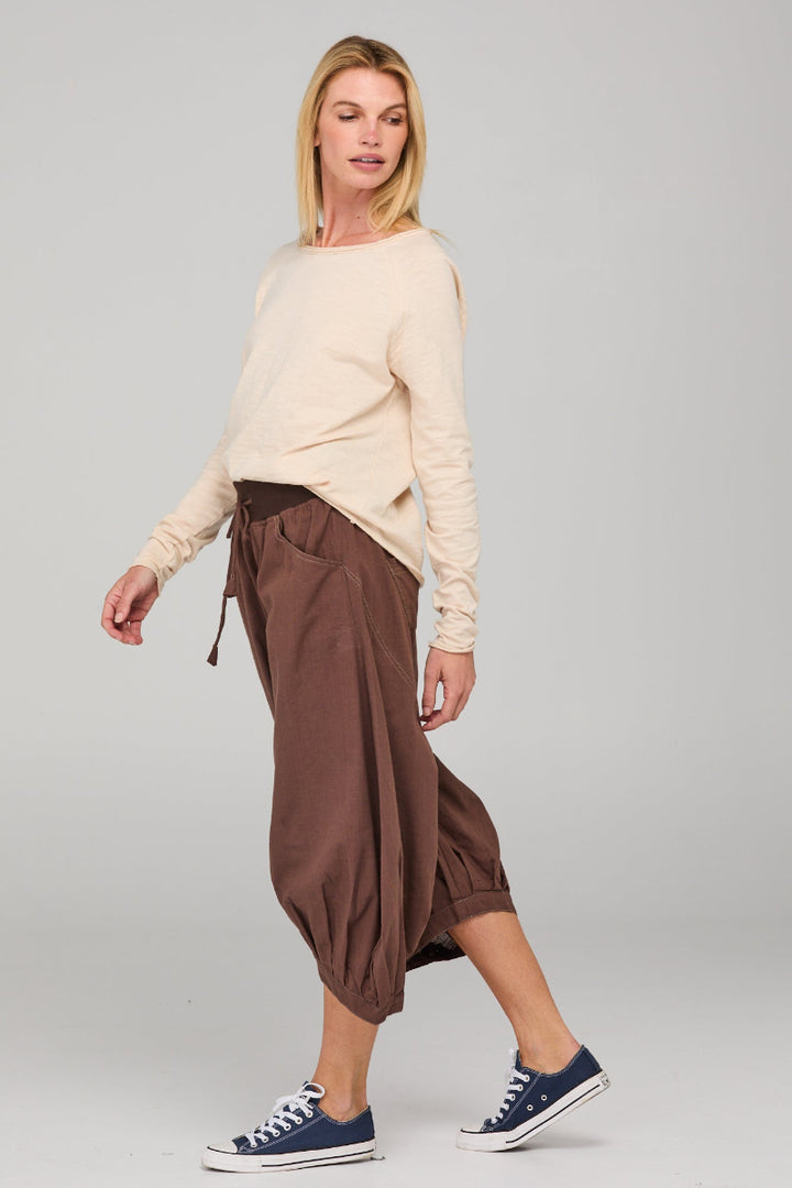 Woman wearing a beige sweater and brown pants on a gray background