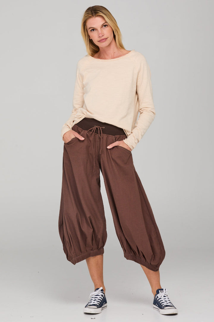 Woman wearing a beige sweater and brown wide-leg pants on a gray background