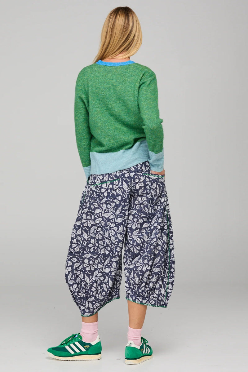 Person wearing a green sweater, light blue shirt, and patterned pants on a gray background
