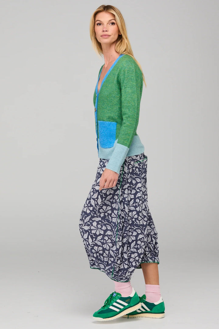 Woman wearing a green cardigan, blue shirt, and patterned skirt on a gray background